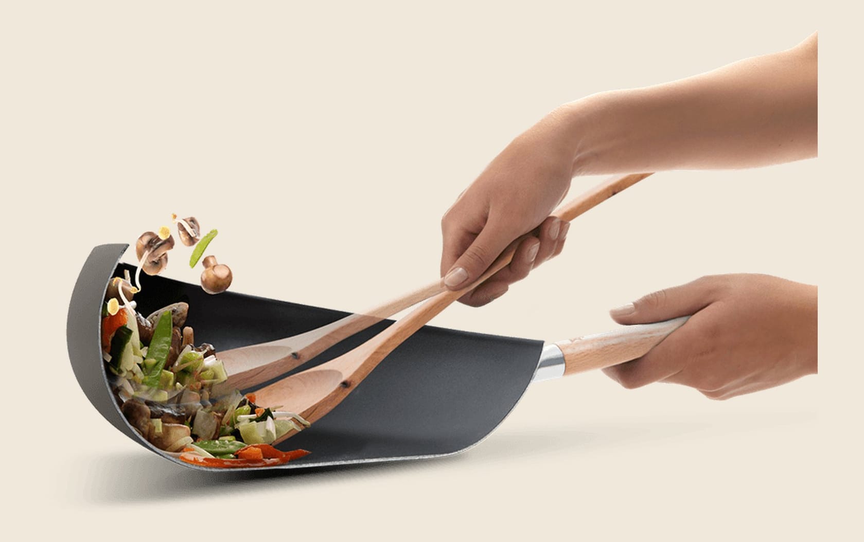 Black wok with high bowl-shaped edge tossing vegetables