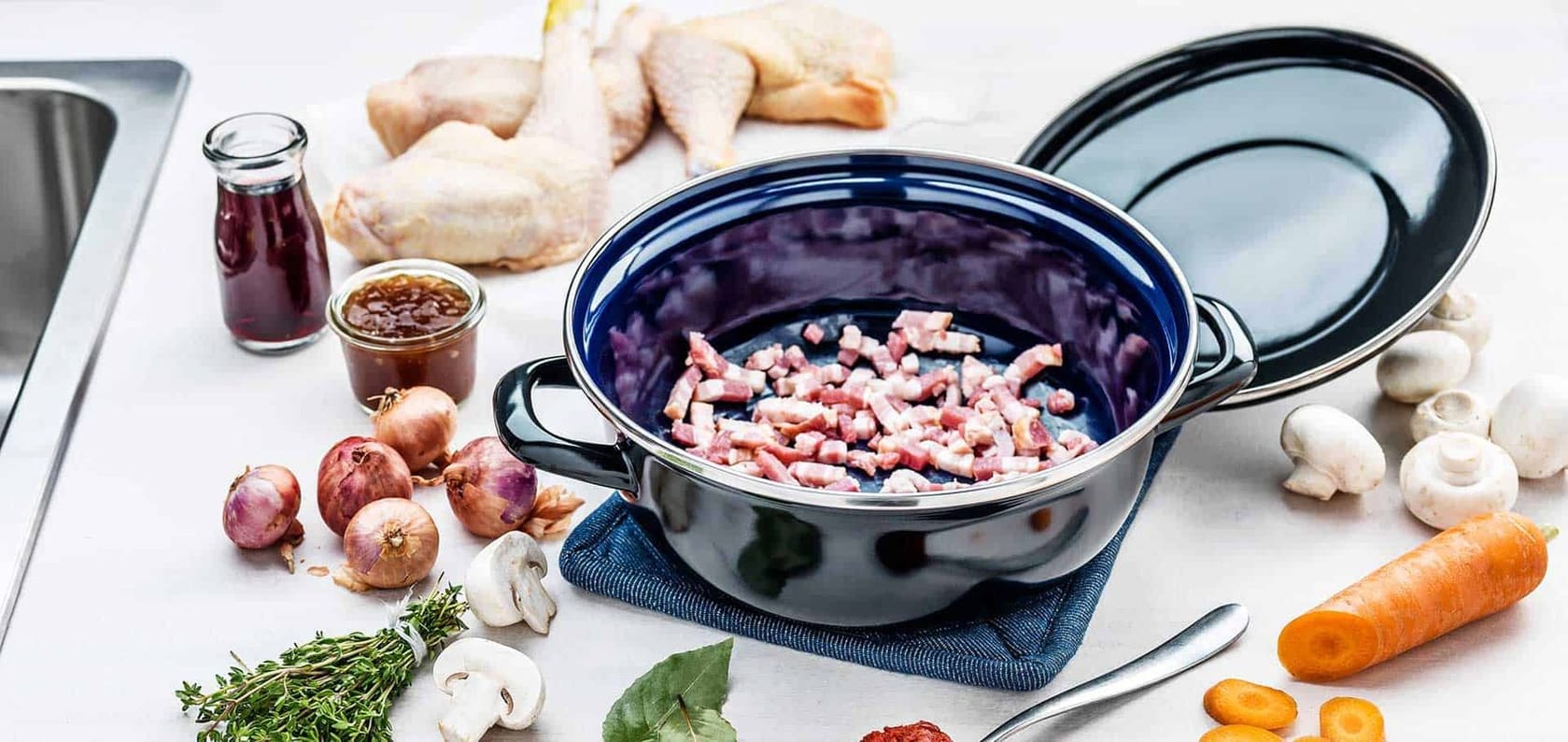 Blue enameled Dutch oven with bacon cooking on a bright kitchen counter