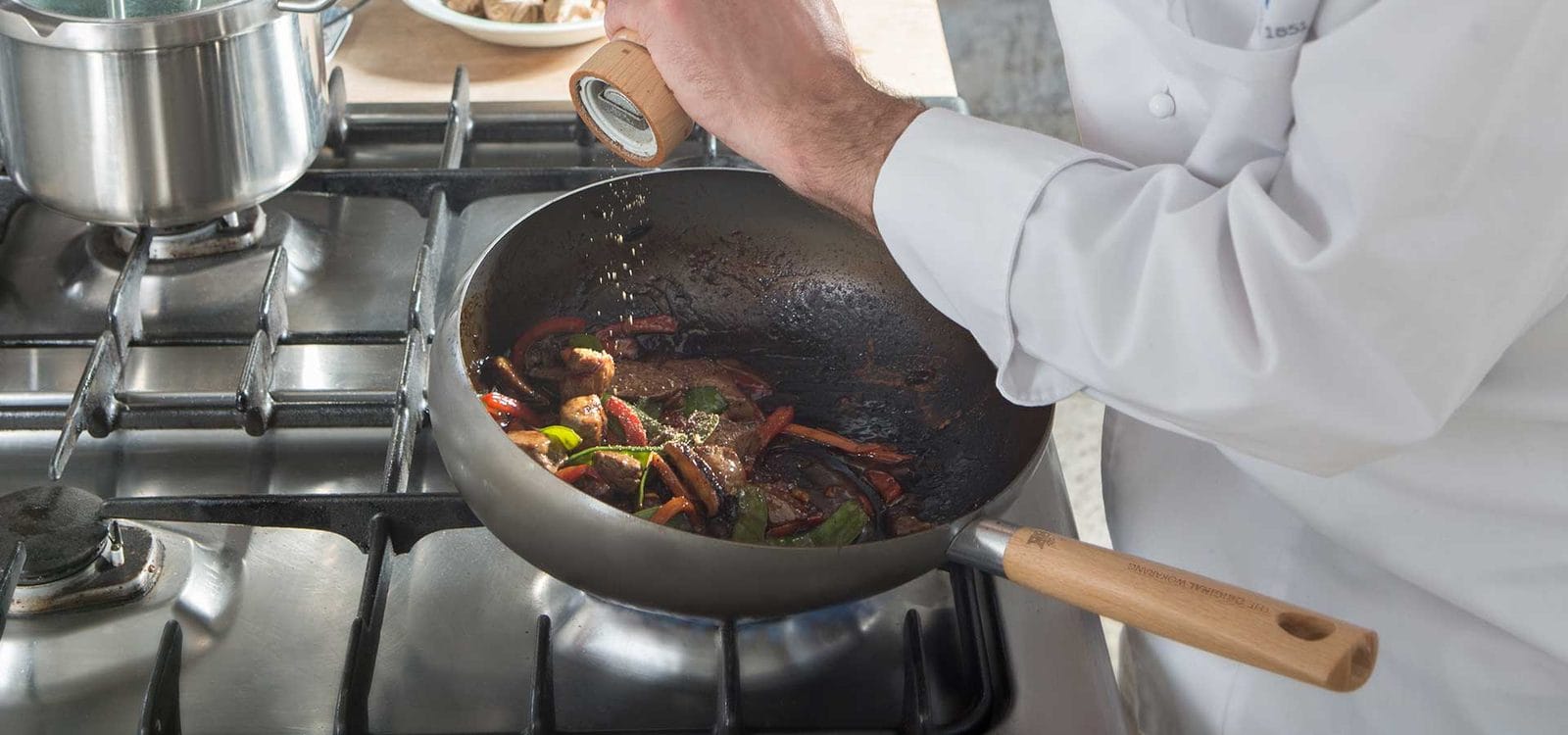 Small enameled Dutch oven simmering on a gas hob while a cook stirs it