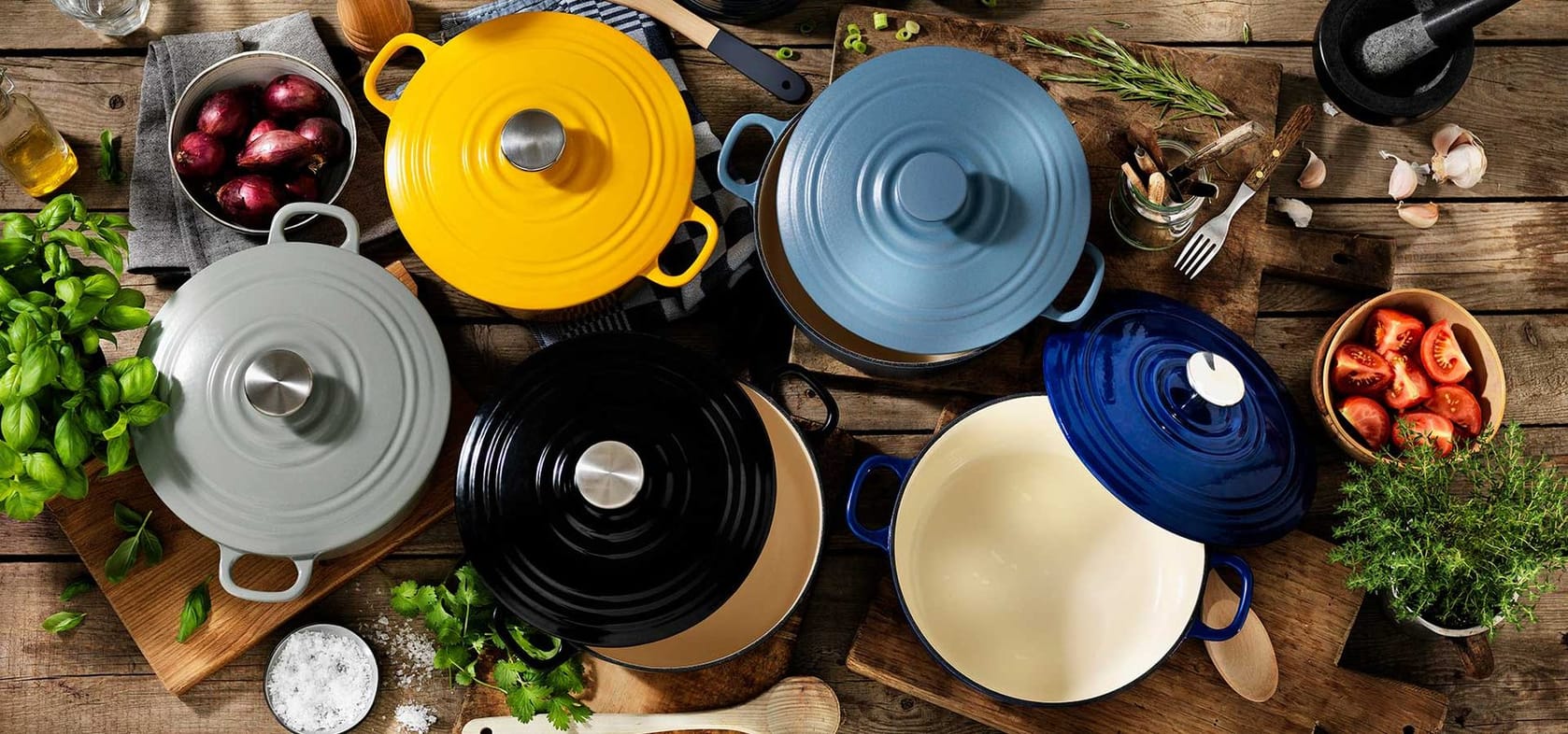 Enameled Dutch ovens in blue, mustard, cream and black arranged around a cutting board