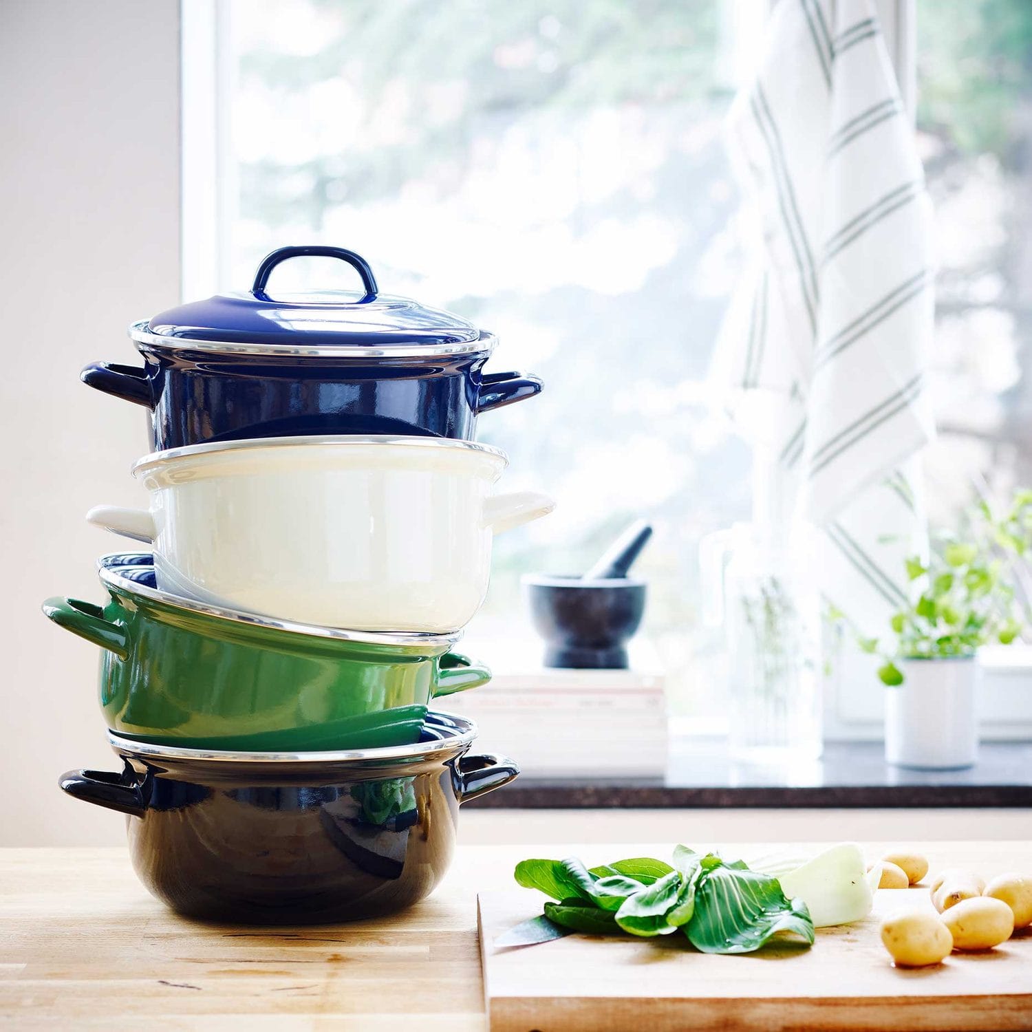Four enameled Dutch ovens stacked tallest to smallest in blue, cream, green and black